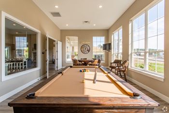 A pool table in a living room with large windows